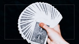 A hand holding a deck of playing cards on a black background.