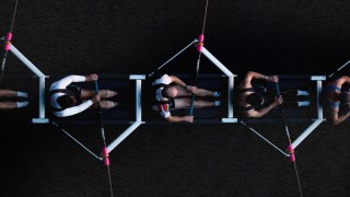 A group of people collaborating and showcasing trust as they sit together on a rope, against a captivating black background.