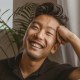 A smiling asian man sitting on a couch.